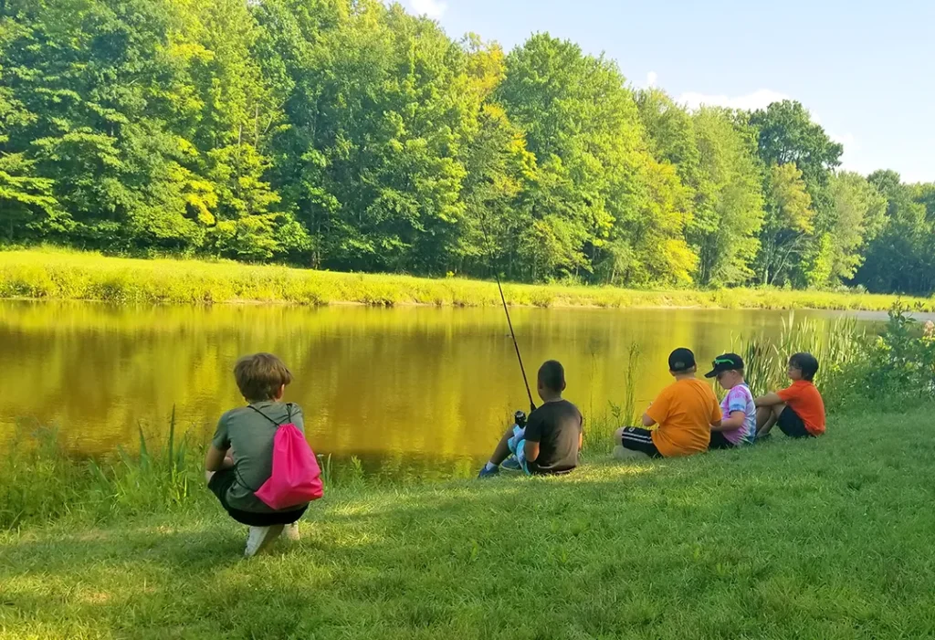 Kids sitting and fishing near a pond at golden hour