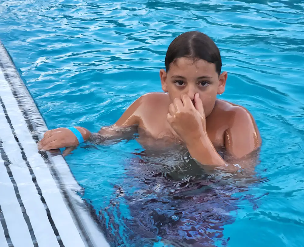 A child plugs his nose getting ready to dunk himself in a swimming pool