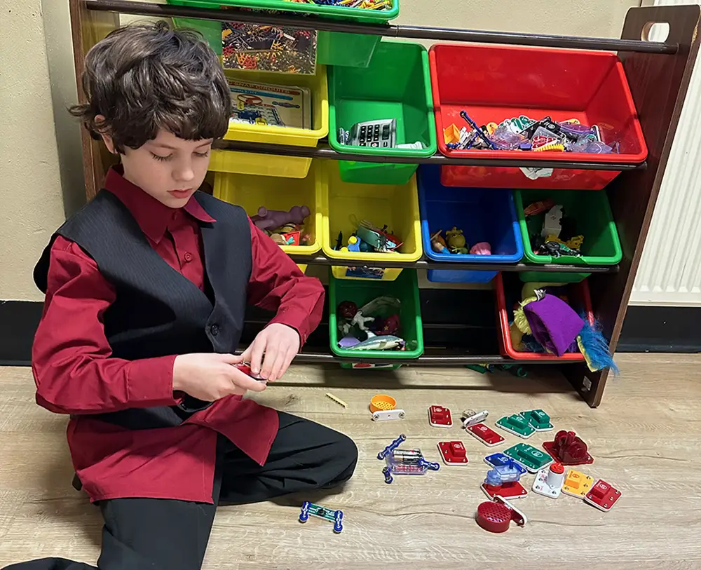 A boy from YA plays with toys next to a colorful stack of toy containers