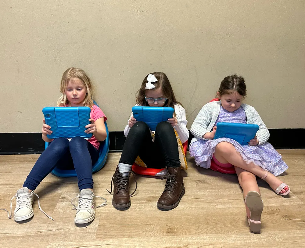 Three girls sitting and leaning back on a while study school materials on blue cased tablets