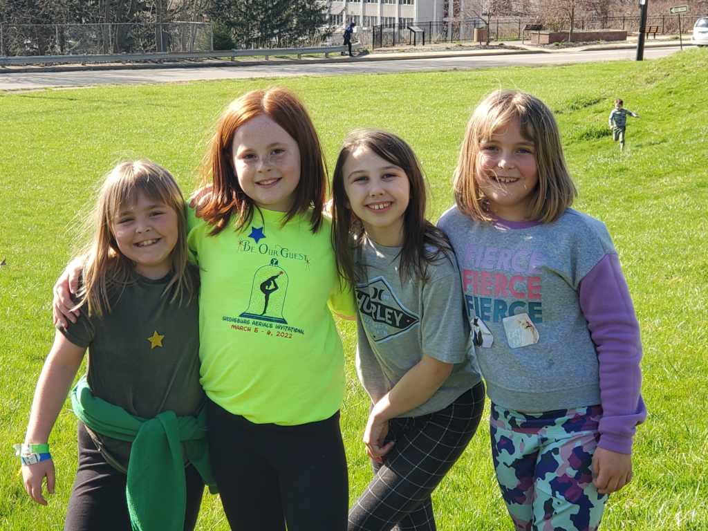 Four girls smiling and holding arms around each other outside of YA on a sunny day